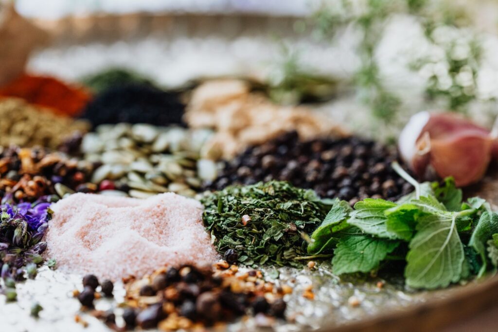 Assorted natural flavor sources including fresh mint, dried herbs, peppercorns, pink salt and seeds spread on a tray