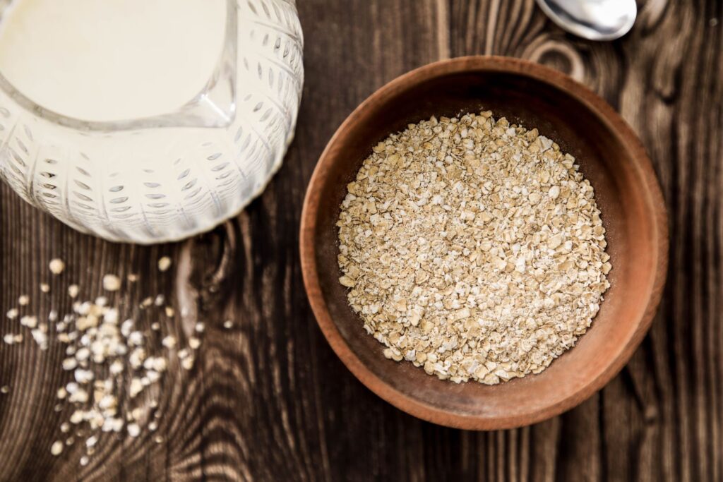 Rolled oats in a wooden bowl beside a jug of milk on a rustic table, illustrating the question of whether oats are gluten fre