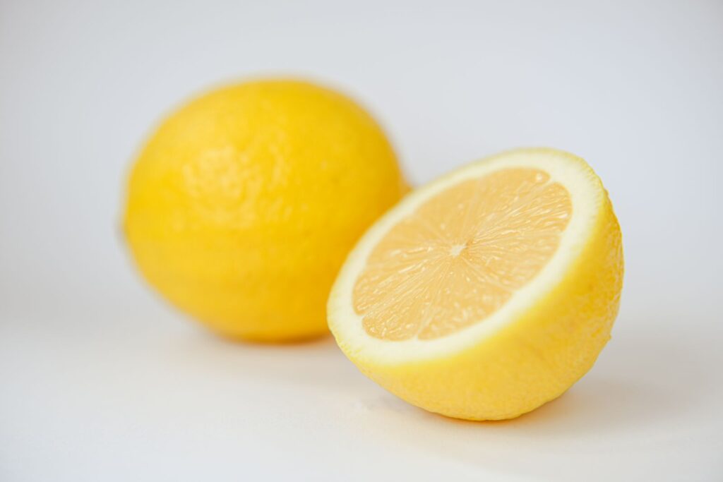 A whole lemon and a halved lemon on a white surface, representing citric acid, the natural acid found in citrus fruit.