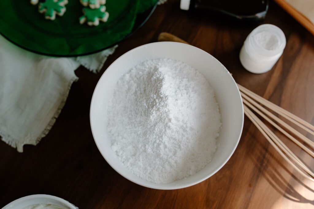 White bowl of fine white powder, like corn starch, on a wooden table beside a whisk, illustrating a gluten-free baking staple