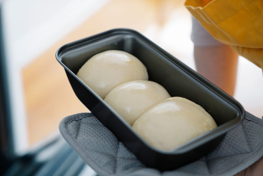 Three smooth balls of proofed dough risen in a loaf pan, showing yeast at work in baking