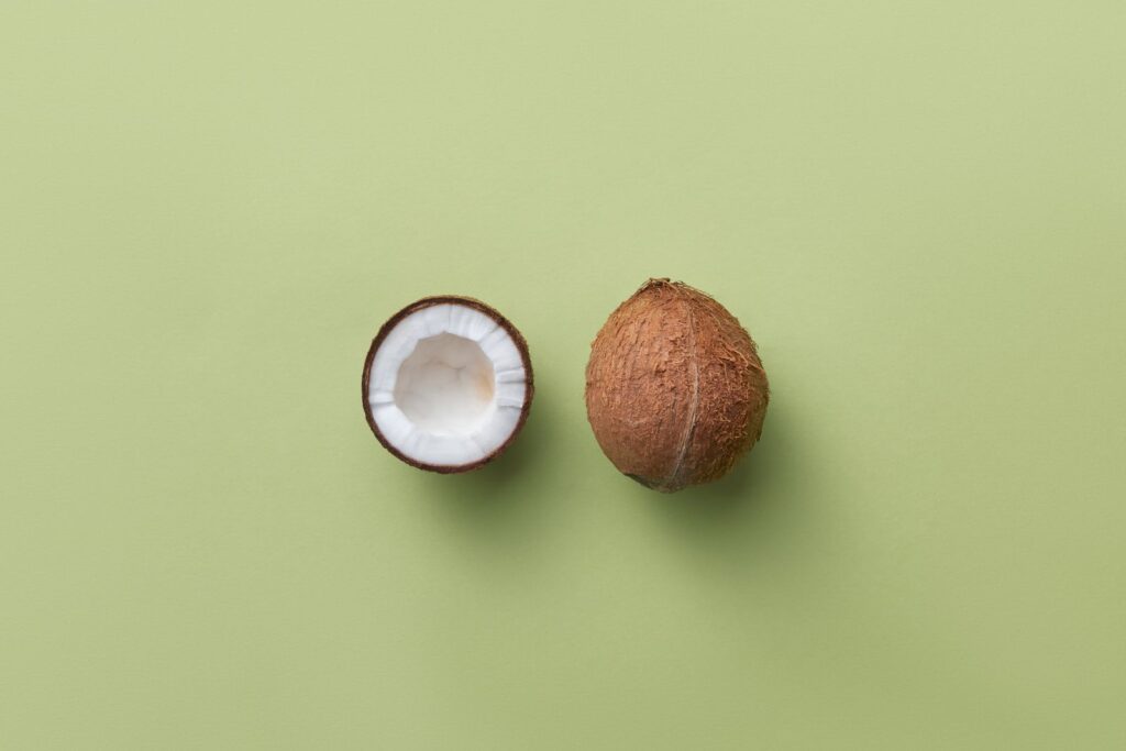 A whole brown coconut next to a halved coconut with white flesh on a green background, the source of gluten-free coconut flou
