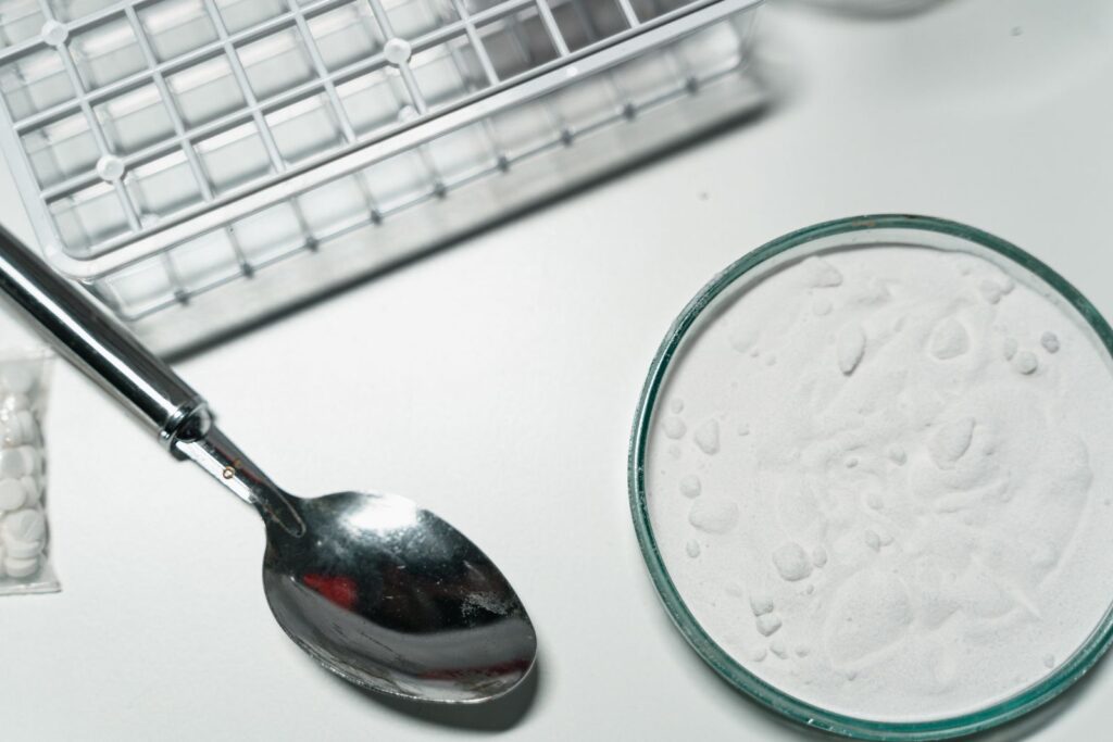 Fine white powder in a glass dish beside a metal spoon and tablets, illustrating dextrin, a powdered additive and thickener.