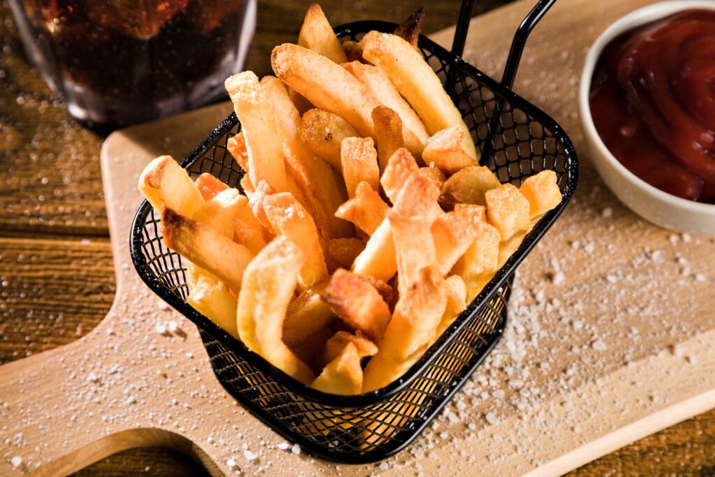 Golden french fries in a wire frying basket on a wooden board with a small bowl of ketchup, illustrating whether fries are gl