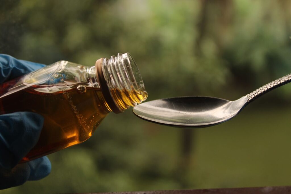 Thick amber syrup pouring from a bottle onto a spoon, illustrating glucose syrup and whether it is gluten free.