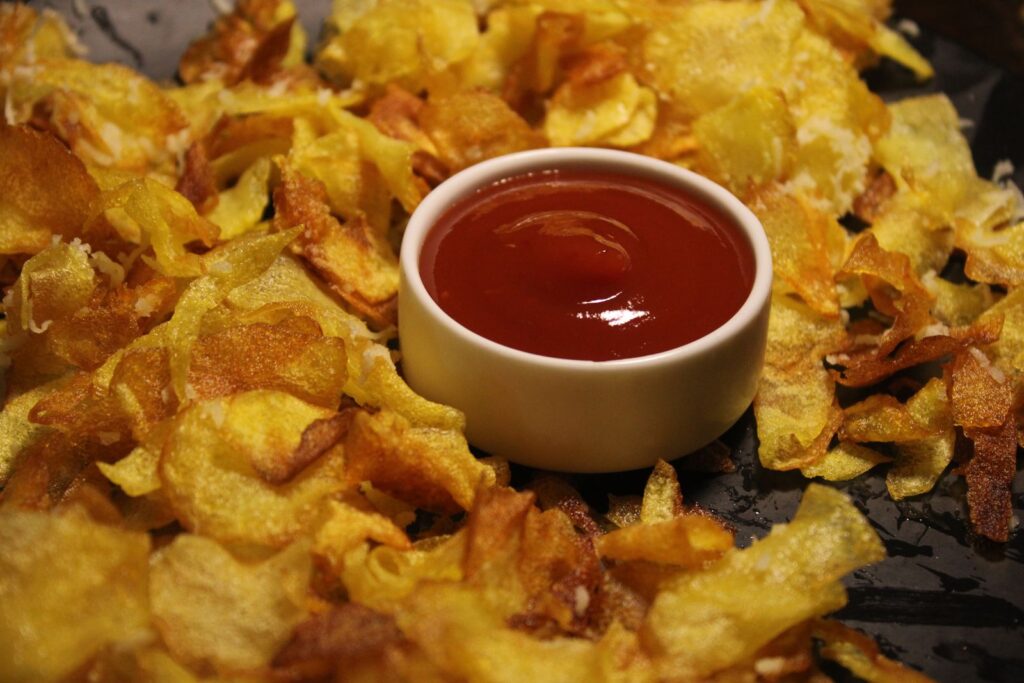 Crispy golden potato chips surrounding a small white bowl of ketchup, illustrating whether potato chips are gluten free.