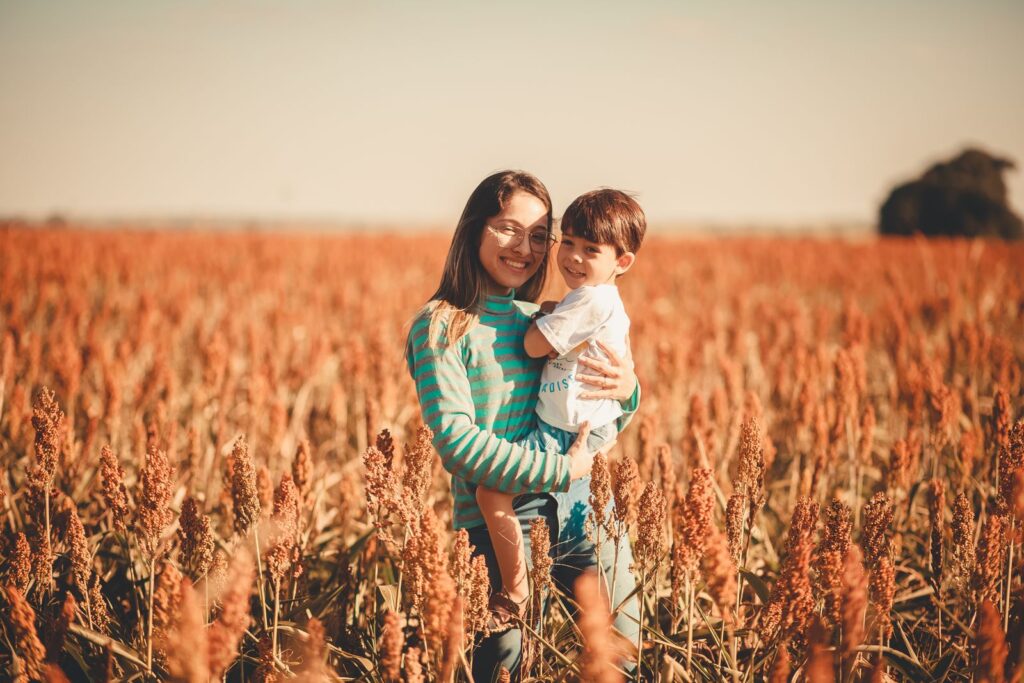 Woman holding a smiling child in a field of ripe orange sorghum, a naturally gluten-free grain