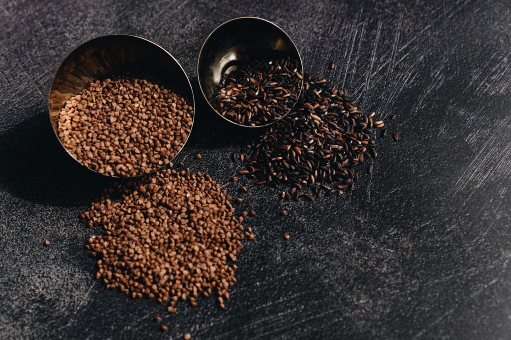 Bowls and scattered piles of tiny brown and dark seeds on a slate surface, showing the small grains of naturally gluten-free