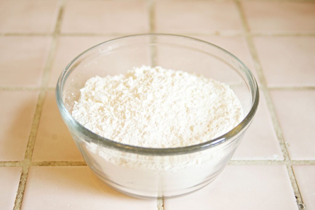 Glass bowl of fine white wheat starch powder on a tiled counter, illustrating the ingredient at the center of the gluten-free